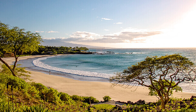 People walking on the beach seen in the distance from a rocky outcropping.